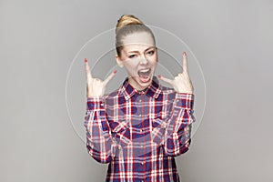 Crazy excited woman with bun hairstyle standing showing rock and roll gesture, screaming.