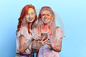 Crazy funny girls with colored faces holding smartphone and posing to the camera