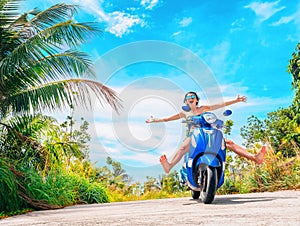 Crazy funny woman with flying hair riding a motorbike on a blue sky and green tropics background. Young bizarre girl