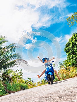 Crazy funny woman with flying hair riding a motorbike on a blue sky and green tropics background. Young bizarre girl