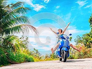 Crazy funny woman with flying hair riding a motorbike on a blue sky and green tropics background. Young bizarre girl