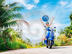 Crazy funny woman with flying hair riding a motorbike on a blue sky and green tropics background. Young girl with dark