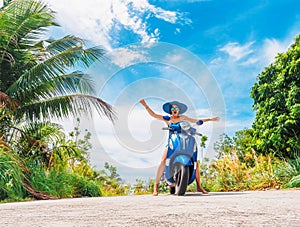 Crazy funny woman with flying hair riding a motorbike on a blue sky and green tropics background. Young girl with dark