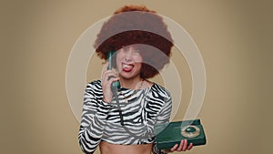 Crazy girl with brown lush wig talking on wired vintage telephone of 80s, fooling making silly faces