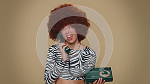Crazy girl with brown lush wig talking on wired vintage telephone of 80s, fooling making silly faces