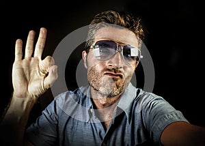 Crazy happy and funny guy with sunglasses and modern hipster look taking selfie self portrait picture with mobile phone camera smi