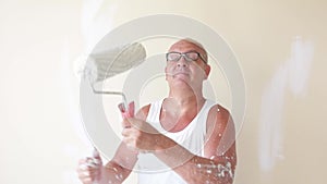 Crazy and happy middle aged man dancing, enjoying and having fun painting by roller interior of the new apartment, home