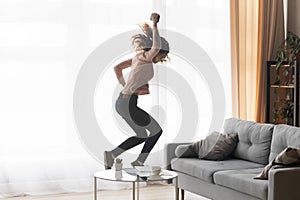 Crazy happy young woman holding cellphone jumps dances alone indoor