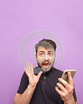 A crazy man with a beard standing on a purple background with a smartphone in his hands, with a shocking face and an open mouth