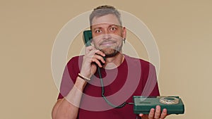 Crazy man in red t-shirt talking on wired vintage telephone of 80s, fooling making silly faces