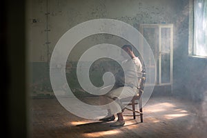 A crazy man in a straitjacket is tied to a chair in an abandoned old clinic photo