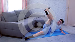 Crazy nerd man is trying to stretch his legs laying on the mat at home. Sport humor concept.