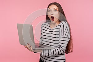 Crazy online study course! Portrait of amazed, surprised woman in striped sweatshirt holding laptop and looking shocked