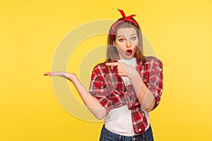 Crazy product advertising. Portrait of amazed pretty pinup girl in checkered shirt pointing at copy space on her palm