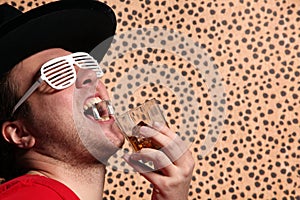 Crazy rock and rollerer with a big black hat, party glasses and a glass of whiskey in front of a cheetah skin background