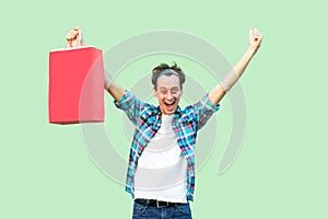 Crazy sale started! Satisfied modern young adult shopoholic man in white t-shirt and checkered shirt triumping with raised hands