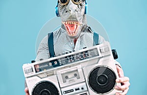 Crazy senior man wearing t-rex mask and listening to music holding vintage boombox stereo outdoor