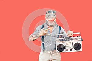 Crazy senior man wearing t-rex mask while listening to music holding vintage boombox stereo outdoor