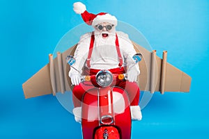 Crazy stylish modern white grey hair bearded santa claus with craft wings drive scooter hurry x-mas party wear red