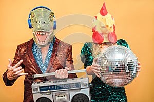 Crazy stylish people listening music with vintage boombox stereo - Fashion couple wearing t-rex and chicken mask at party fest