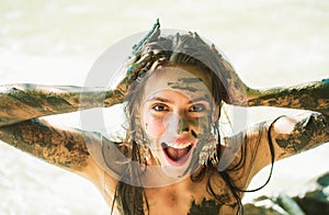 Crazy woman is laughing as he plays outside in the mud and rubs dirt on his face with his hands.