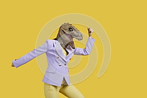 Crazy woman with with t-rex mask threatening someone with her fist, copy space for text on yellow background . Studio