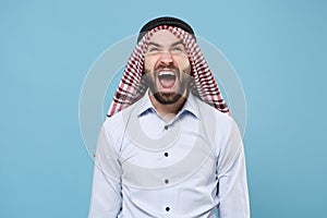 Crazy young bearded arabian muslim man in keffiyeh kafiya ring igal agal casual clothes  on pastel blue photo