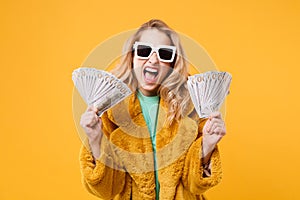 Crazy young blonde woman girl in yellow fur coat, dark sunglasses isolated on orange background. People lifestyle