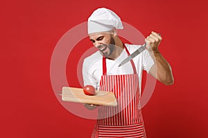 Crazy young male chef cook or baker man in striped apron toque chefs hat posing isolated on red background. Cooking food