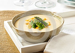 Cream of asparagus soup in a bowl on a wooden tray.