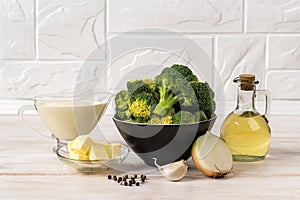 Cream of broccoli soup raw ingredients on the countertop. Puree soup recipe of broccoli florets, garlic, onion, cream, butter,