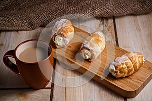 Cream cakes on a wooden plate with a cup of coffee with milk. The concept of natural and delicious food.