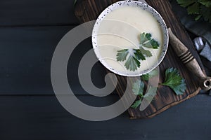 Cream of cauliflower soup with cream and greens, in a white cup on a wooden board and black background. Vintage photo. Fresh