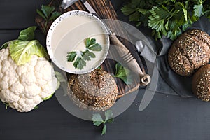 Cream of cauliflower soup with cream and greens, in a white cup on a wooden board and black background. Vintage photo. Fresh