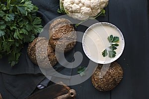 Cream of cauliflower soup with cream and greens, in a white cup on a wooden board and black background. Vintage photo. Fresh