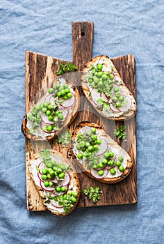 Cream cheese, green peas, radishes and micro greens spring sandwiches on a cutting board. Healthy eating, slimming, diet lifestyle