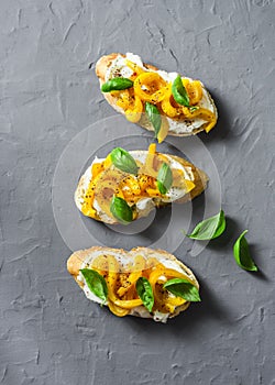 Cream cheese, roasted yellow bell pepper, basil bruschetta on on grey background, top view. Copy space