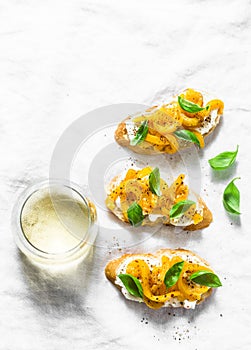 Cream cheese, roasted yellow bell pepper, basil bruschetta and white wine on light background, top view. Flat lay