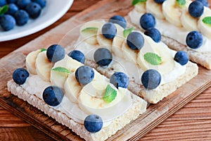 Cream cheese sandwiches idea. Vegetarian crusty bread sandwiches with cheese cream, bananas and berries on wooden board