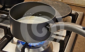 Cream is cooked in saucepan on gas stove to make cake