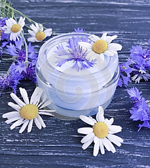cream cosmetic flowers cornflower, product essence camomile alternative on a dark wooden background