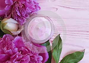 Cream cosmetic, peony flower on a pink wooden background