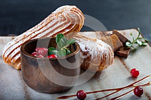Cream eclairs choux pastries served with fresh cranberries on a handmade ceramic plate. Profiterole cupcakes