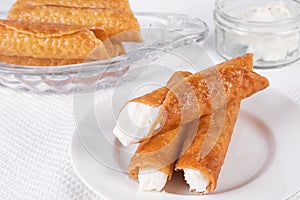 Cream filled brandy snaps, unfilled snaps and a pot with cream