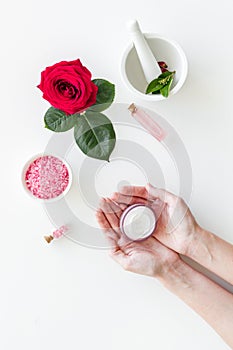 Cream in hands, bath salt, lotion for organic cosmetics with rose flower on white background top view