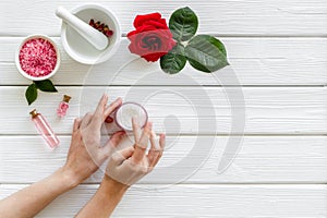 Cream in hands, bath salt, lotion for organic cosmetics with rose flower on white wooden background top view copyspace