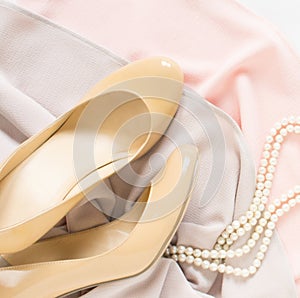 Cream heeled women`s shoes, pink dress and pearls necklace on white background.