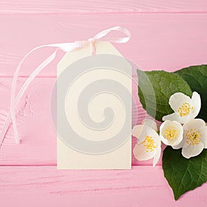 Cream label & jasmine flowers on pastel pink wood table.