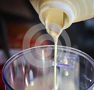 The cream is poured from a plastic bottle into a bowl