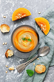 Cream of pumpkin soup served with toasted bread on a gray background. View from above, flat lay